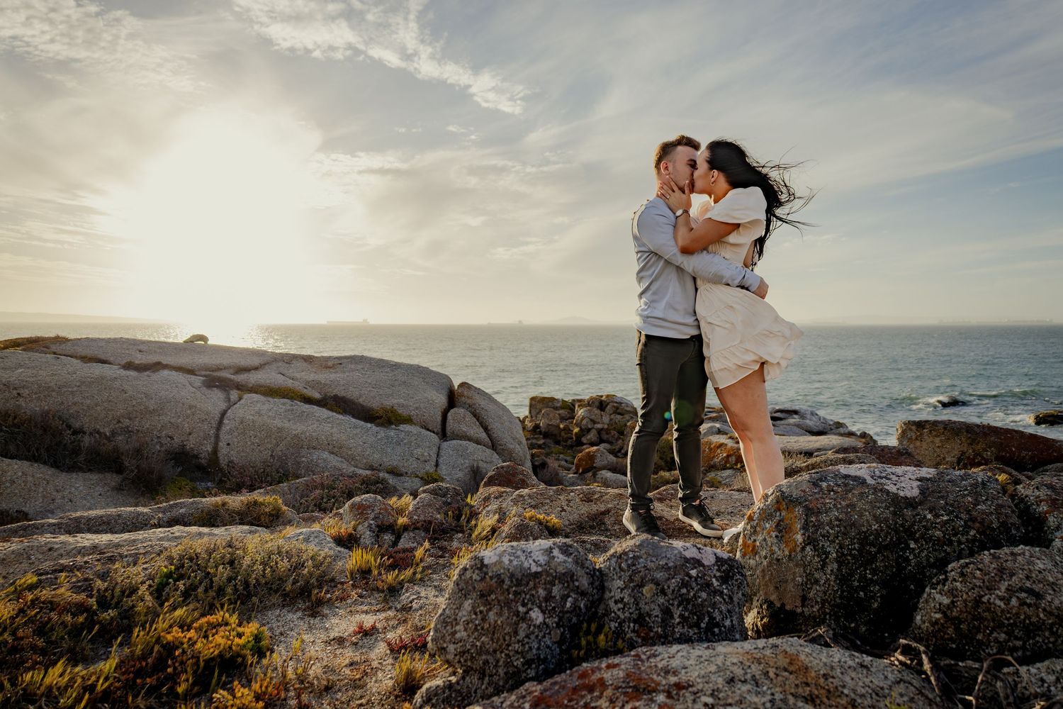 Couple kissing on a rocky shoreline at sunset