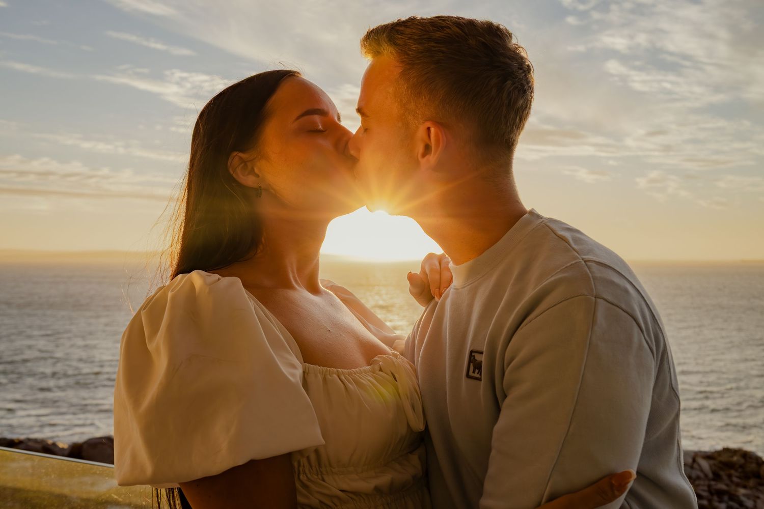 Couple kissing in front of a sunset over the ocean
